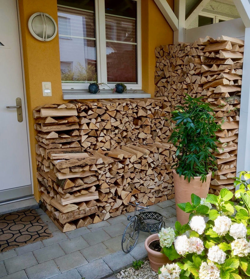 Aufgeschichtetes Brennholz an einer Hauswand unter einem Vordach